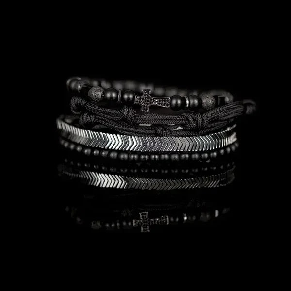 Black layered men’s bracelet with matte beads, braided cord knots, silver-tone chevron accents, and pavé cross centerpiece on a white background.