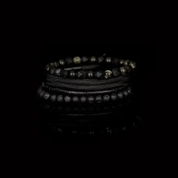 Layered men’s bracelet set featuring black lava stone beads, faceted black stone beads, braided black cord wraps, and metallic hematite accents in a monochromatic stacked design, displayed on a white background.