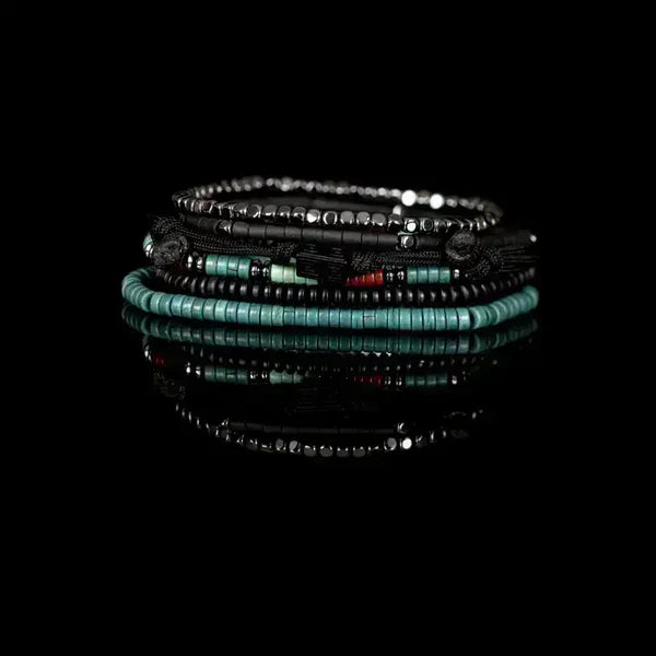 Layered men’s bracelet set featuring black hematite beads, turquoise and coral heishi bead accents, black braided cord details, and geometric metal elements, displayed on a white background.