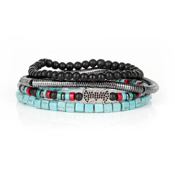 Layered men’s bracelet set featuring turquoise cube beads, black matte stone beads, silver-tone hematite beads, colorful accent beads, and a crystal pavé bat centerpiece, displayed on a white background.
