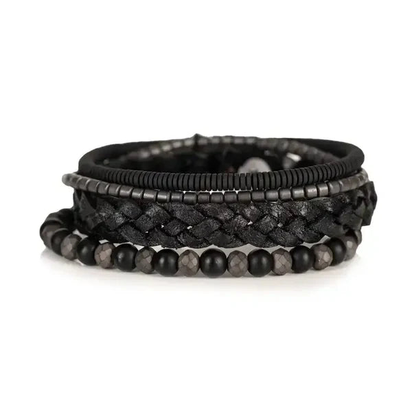 Layered men’s bracelet set featuring a braided black leather band, matte black beads, faceted hematite beads, and hematite disc accents in a monochromatic stacked design, displayed on a white background.