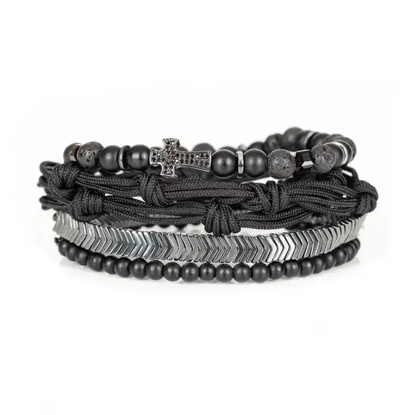 Black layered men’s bracelet with matte beads, braided cord knots, silver-tone chevron accents, and pavé cross centerpiece on a white background.