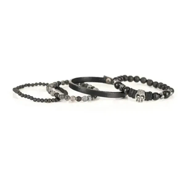 Layered men’s bracelet set featuring black faceted stone beads, a black leather band, lava stone beads, gray natural stone beads, and a silver skull centerpiece, displayed on a white background.