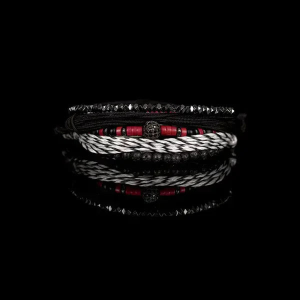 Layered men’s bracelet set featuring black braided cord, red heishi beads, faceted hematite beads, black lava stone beads, a black-and-white woven bracelet, and a pavé crystal centerpiece, displayed on a white background.