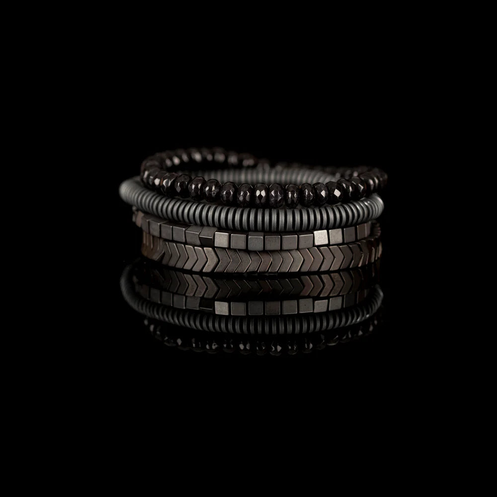 Men's handcrafted layered bracelet set featuring faceted black hematite beads, matte gray heishi disc beads, polished hematite cube beads, and black hematite arrow-shaped beads. Premium minimalist men's bracelet stack photographed on a clean white background.