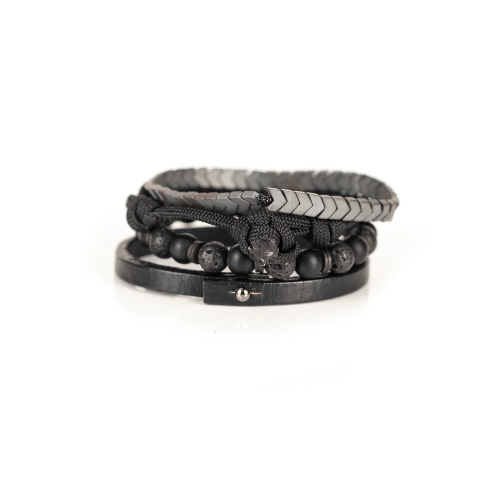 Men's handcrafted layered bracelet set featuring matte black onyx beads, black lava stone beads, black braided cord, genuine black leather band, and gunmetal hematite arrow-shaped beads. Premium minimalist men's bracelet stack photographed on a clean white background.