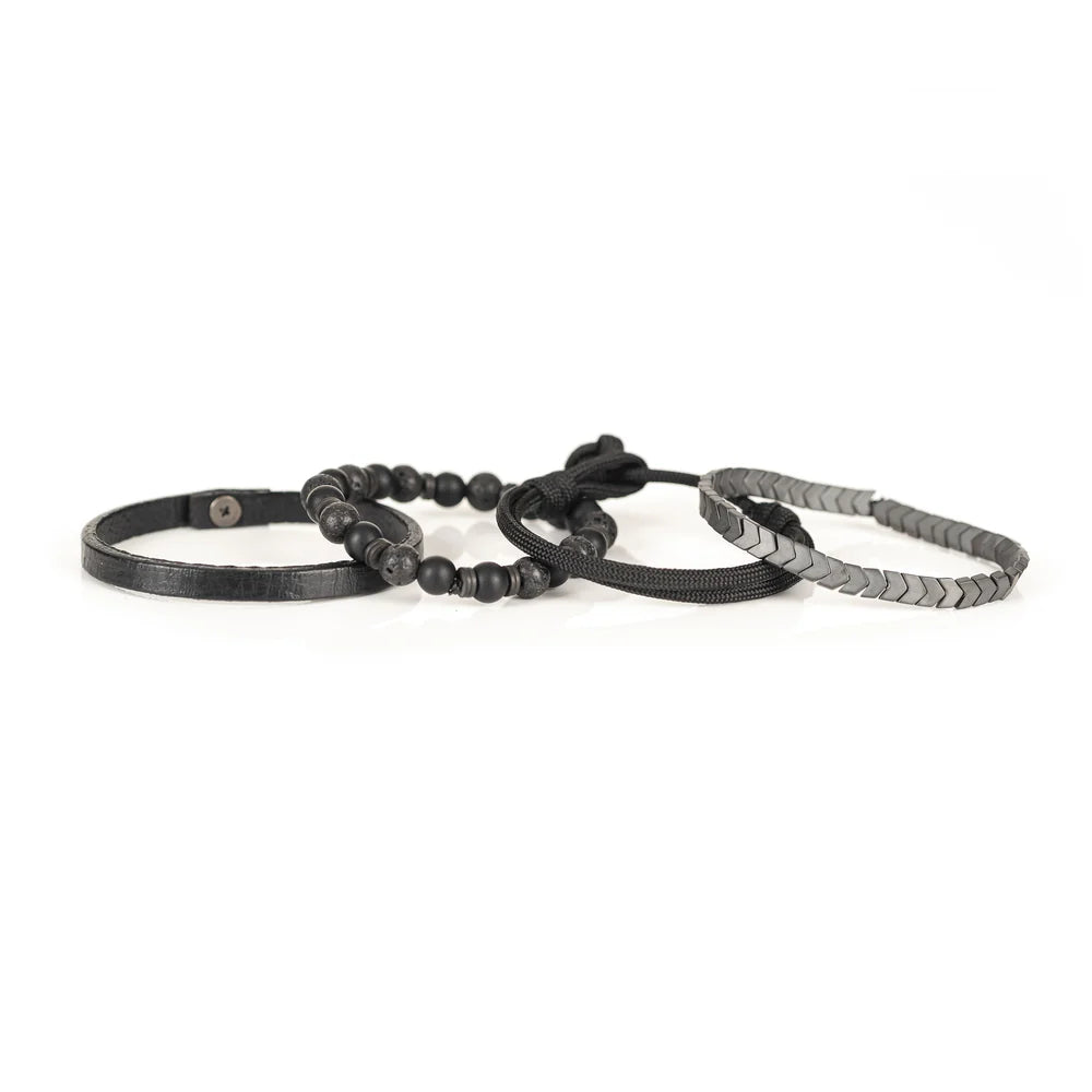 Men's handcrafted layered bracelet set featuring matte black onyx beads, black lava stone beads, black braided cord, genuine black leather band, and gunmetal hematite arrow-shaped beads. Premium minimalist men's bracelet stack photographed on a clean white background.