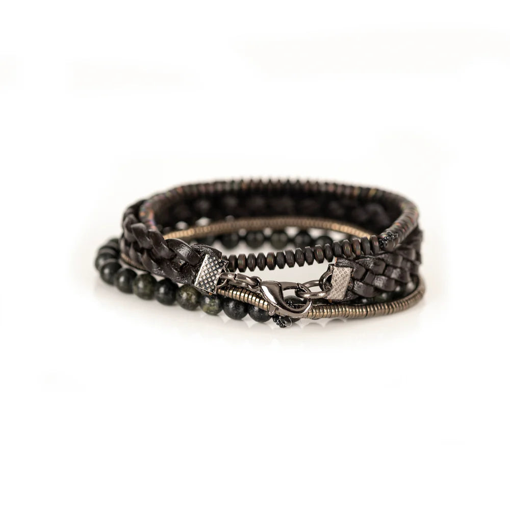 Men's handcrafted layered bracelet set featuring a dark brown braided genuine leather bracelet, natural green serpentine gemstone beads, bronze hematite heishi beads, and metallic spacer beads. Premium artisan men's bracelet stack photographed on a clean white background.