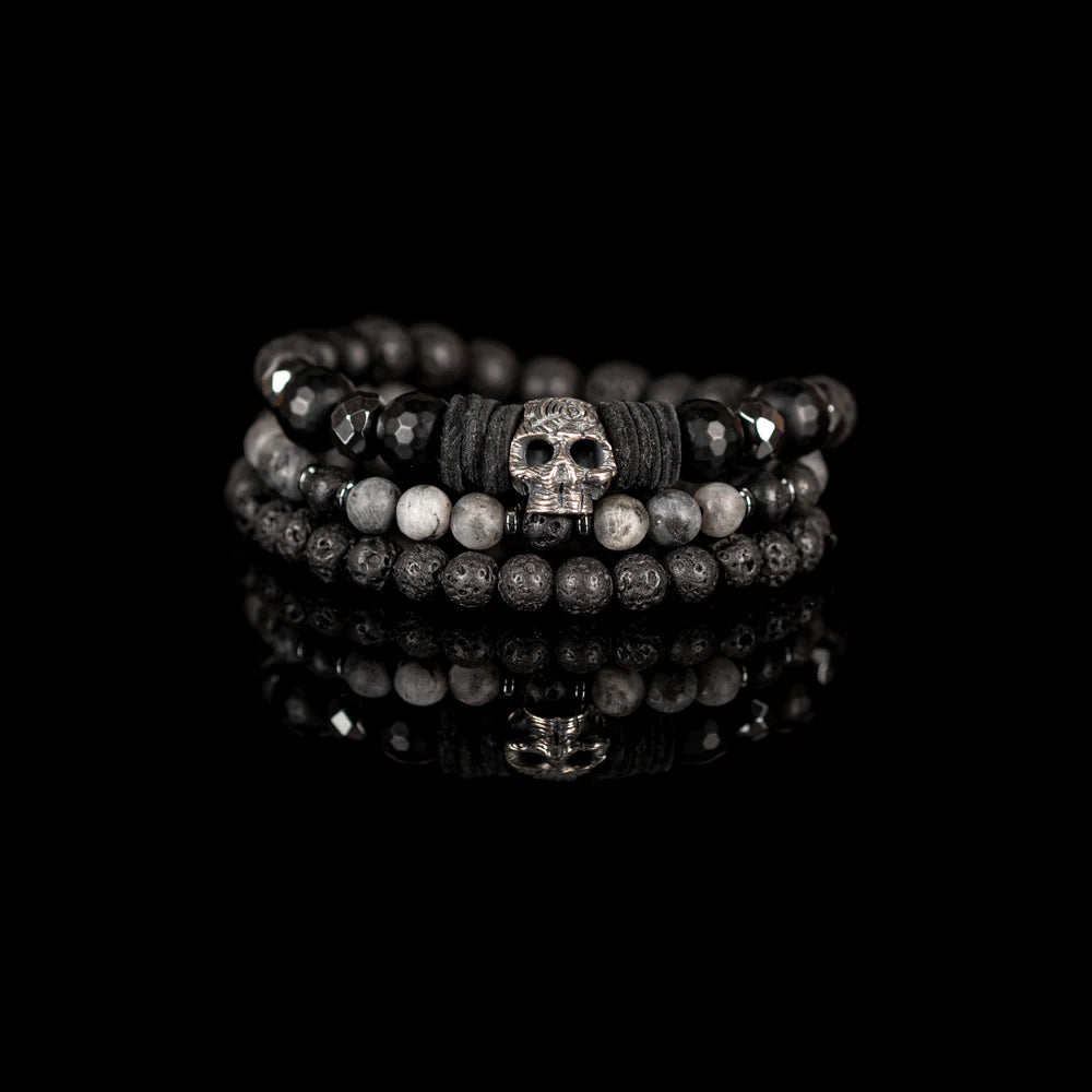 Men's handcrafted layered bracelet set featuring faceted black onyx beads, black lava stone beads, natural gray jasper gemstone beads, black hematite spacer beads, and a silver skull centerpiece with black leather accents. Premium stacked men's bracelet photographed on a clean white background.