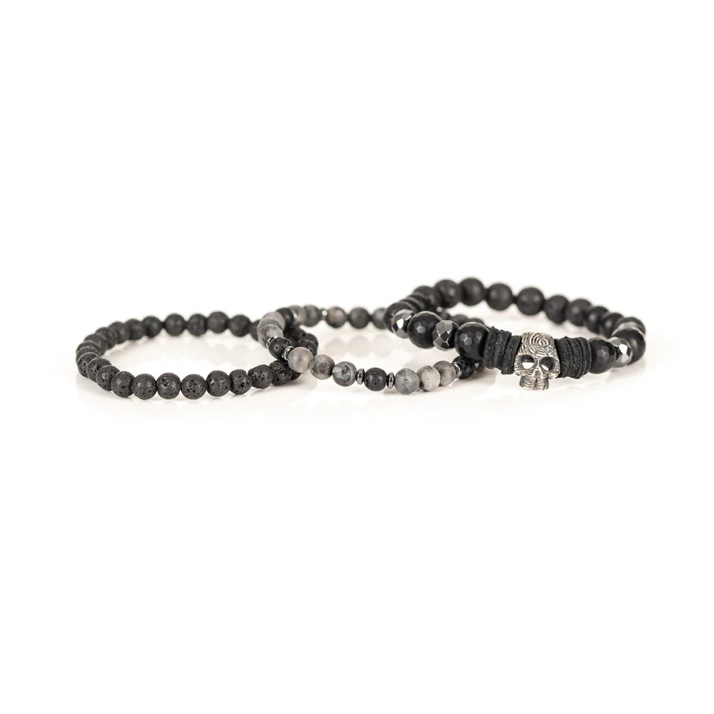Men's handcrafted layered bracelet set featuring faceted black onyx beads, black lava stone beads, natural gray jasper gemstone beads, black hematite spacer beads, and a silver skull centerpiece with black leather accents. Premium stacked men's bracelet photographed on a clean white background.
