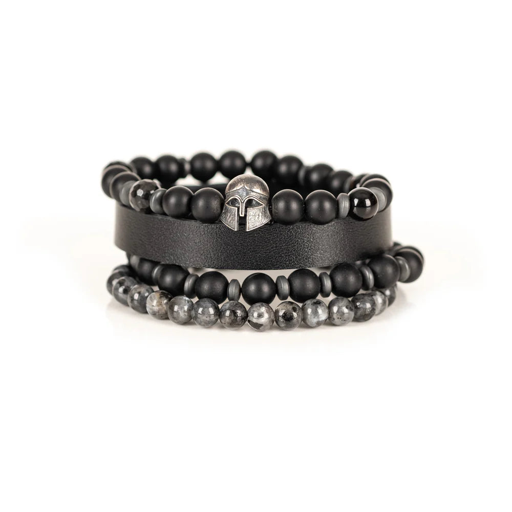 Men's handcrafted layered bracelet set featuring a black genuine leather cuff, matte black onyx beads, faceted black hematite beads, natural gray jasper gemstone beads, black hematite spacer beads, and a silver Spartan helmet centerpiece. Premium stacked men's bracelet photographed on a clean white background.