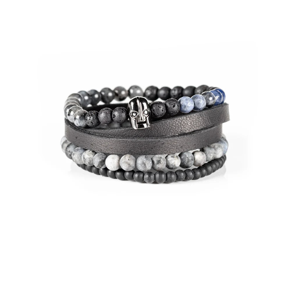 Men's handcrafted black leather wrap bracelet set featuring matte black onyx beads, natural gray jasper stone beads, black lava stone, blue sodalite accent beads, and a polished black skull centerpiece. Premium layered men's bracelet stack photographed on a clean white background.
