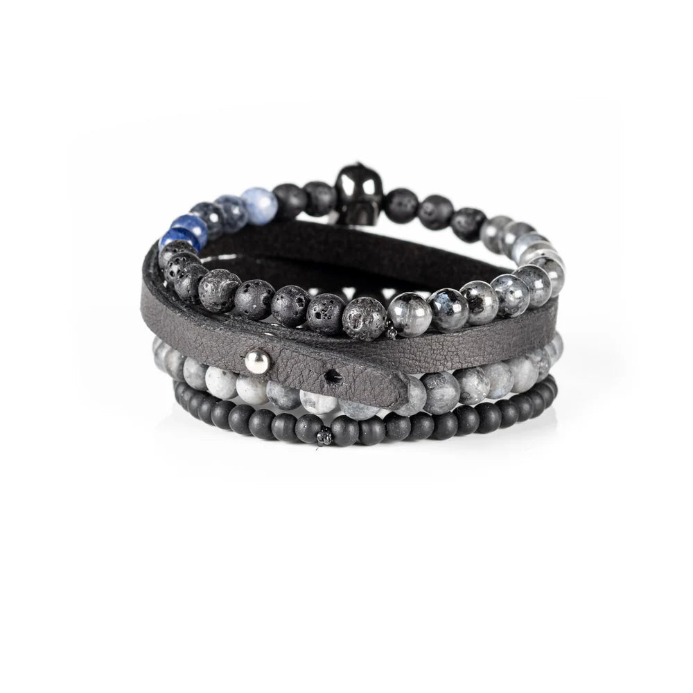 Men's handcrafted black leather wrap bracelet set featuring matte black onyx beads, natural gray jasper stone beads, black lava stone, blue sodalite accent beads, and a polished black skull centerpiece. Premium layered men's bracelet stack photographed on a clean white background.