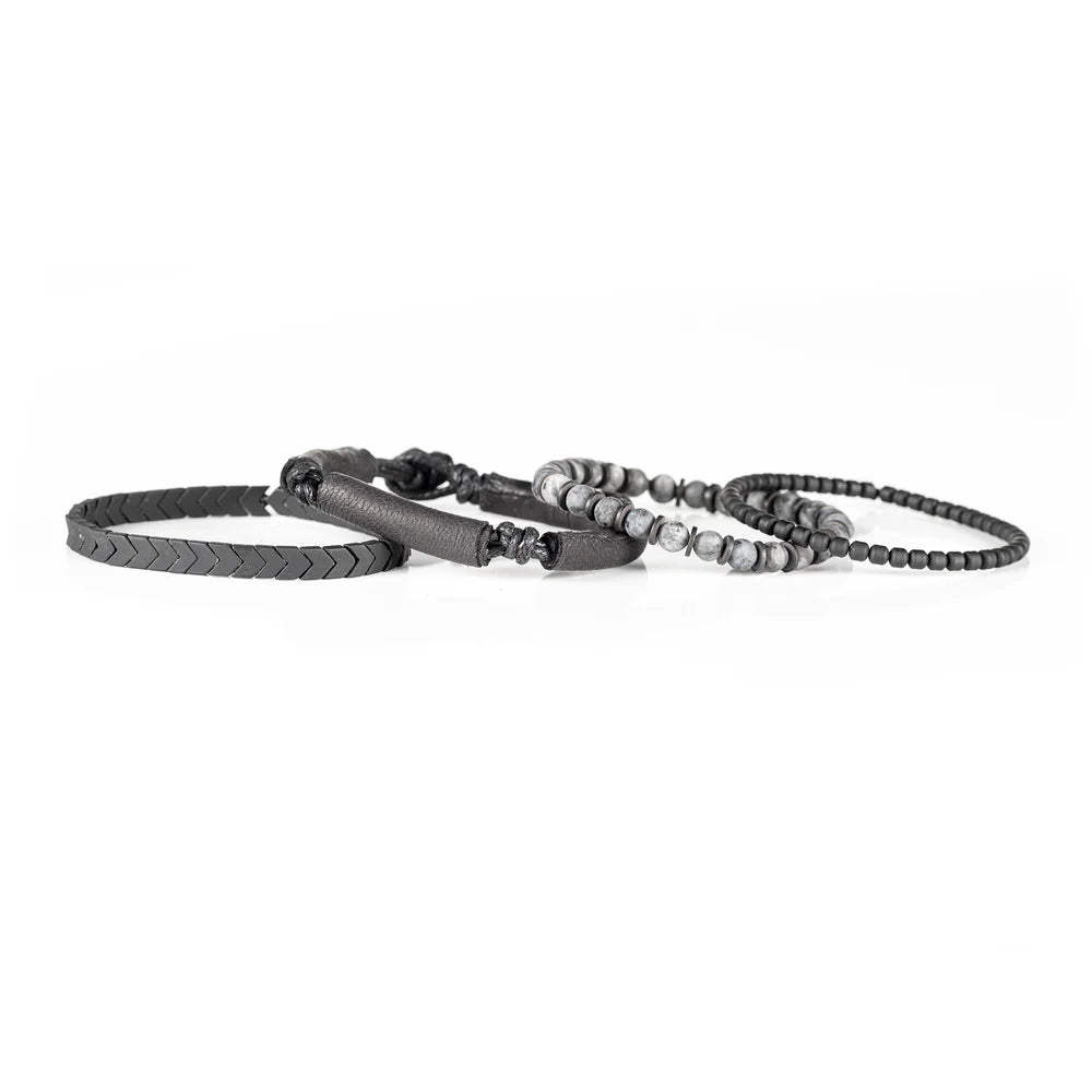 Men's handcrafted layered bracelet set featuring black leather wrap bands, matte black hematite arrow beads, black seed beads, and natural gray jasper gemstone beads. Premium stacked men's bracelet with minimalist design photographed on a clean white background.