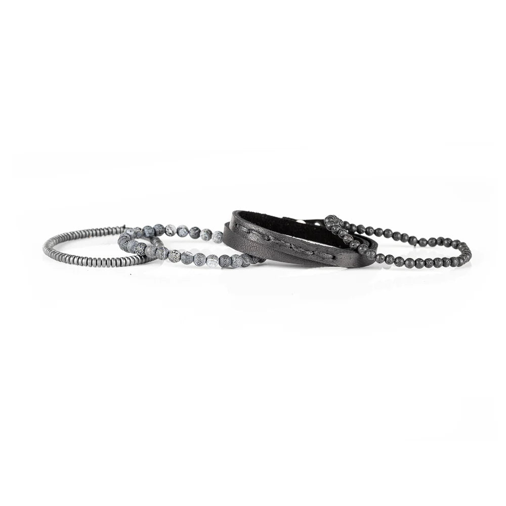 Men's handcrafted layered bracelet set featuring a black genuine leather wrap cuff, black lava stone beads, natural gray crackle agate gemstone beads, matte gray heishi disc beads, and premium stitched leather detailing. Luxury men's stacked bracelet photographed on a clean white background.
