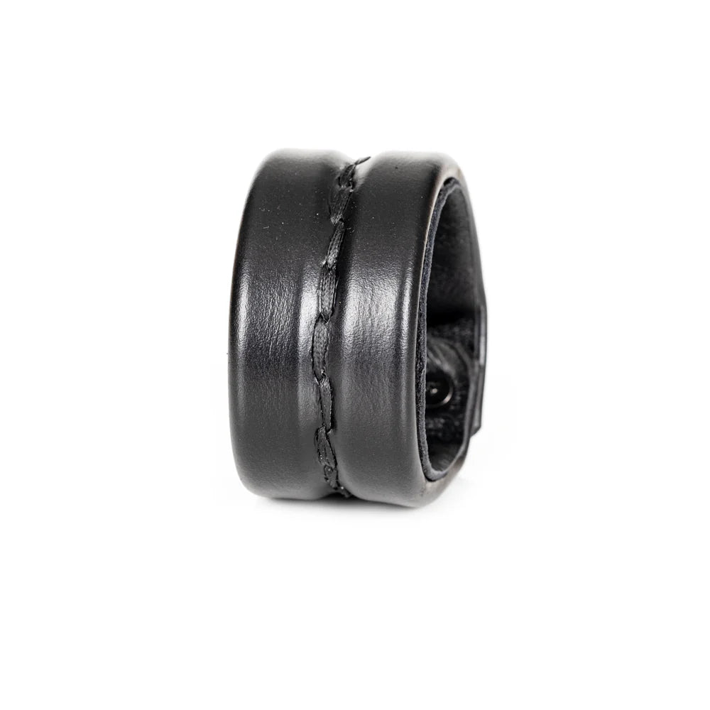 Black genuine leather cuff bracelet with a wide padded silhouette and handcrafted center stitching detail, minimalist statement accessory on a white background.