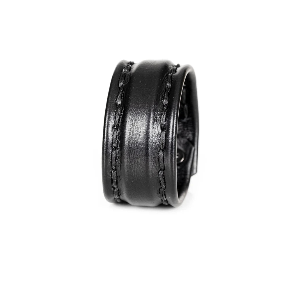 Black genuine leather cuff bracelet with a wide padded center panel and hand-stitched leather straps, photographed on a black reflective background with a luxury editorial look.