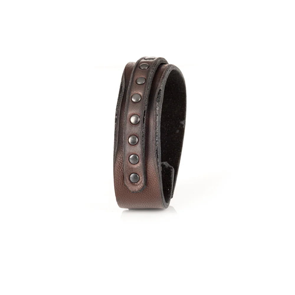 Men's handcrafted genuine leather cuff bracelet in dark brown featuring a wide minimalist design with a slim leather strip accented by matte black metal studs. Premium artisan men's leather wristband photographed on a clean white background.
