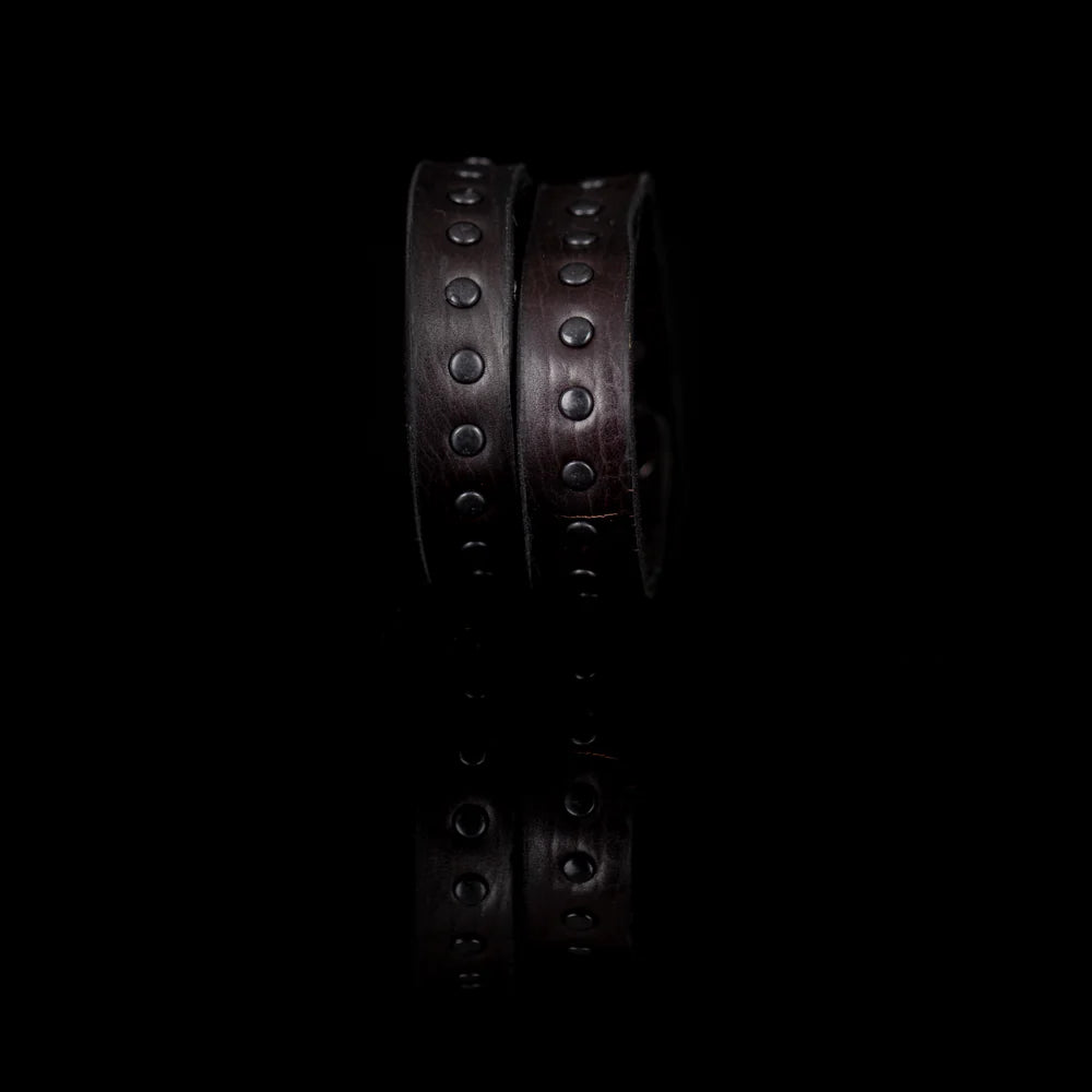 Black genuine leather wrap bracelet featuring double leather bands with black rivet detailing, handcrafted statement accessory with a rugged minimalist design, displayed on a white background.