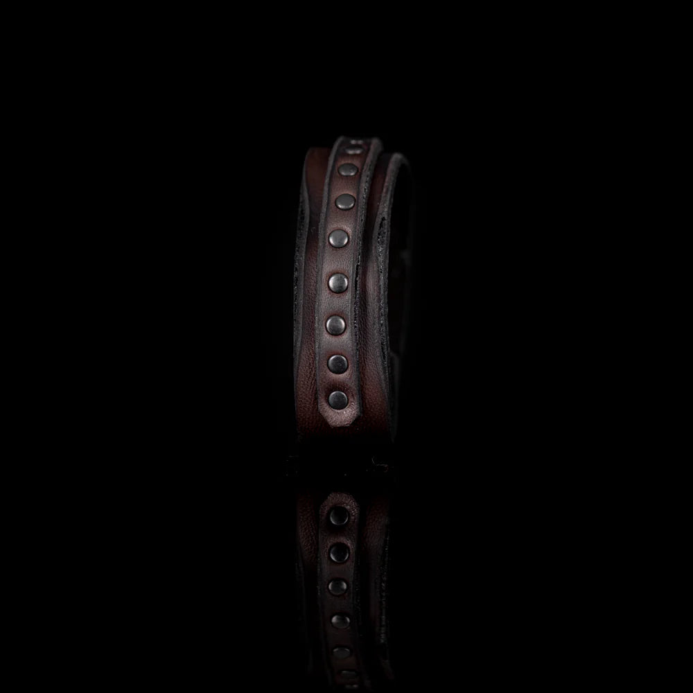 Men's handcrafted genuine leather cuff bracelet in dark brown featuring a wide minimalist design with a slim leather strip accented by matte black metal studs. Premium artisan men's leather wristband photographed on a clean white background.