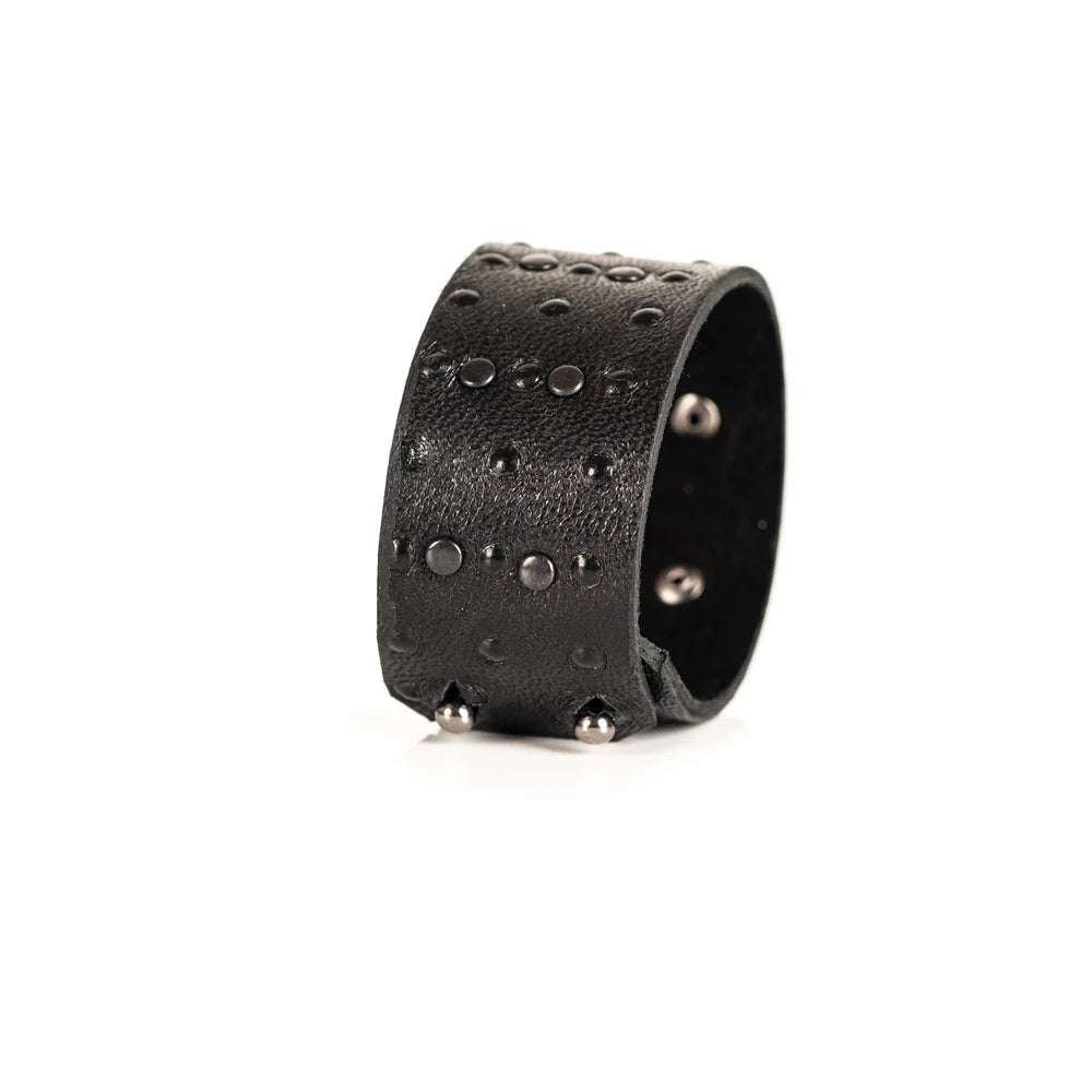 Black genuine leather cuff bracelet with black stud detailing arranged in a geometric pattern, handcrafted statement accessory with a textured leather finish on a white background.