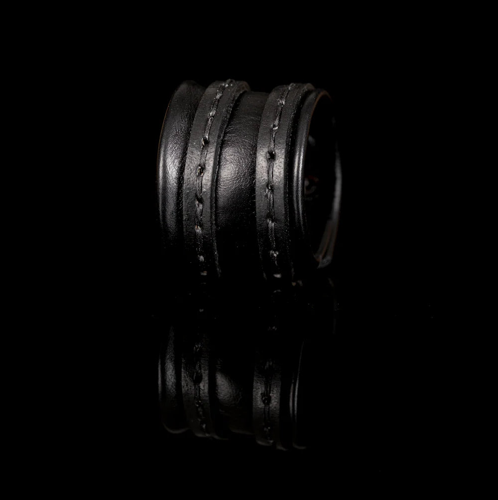 Black genuine leather cuff bracelet with a wide padded center band and hand-stitched wrap straps, handcrafted minimalist statement accessory on a white background.