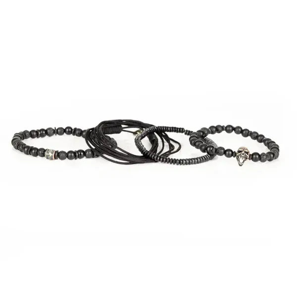 Black layered men’s bracelet with matte black beads, lava stone accents, braided cord wraps, and an antique silver skull centerpiece on a white background.