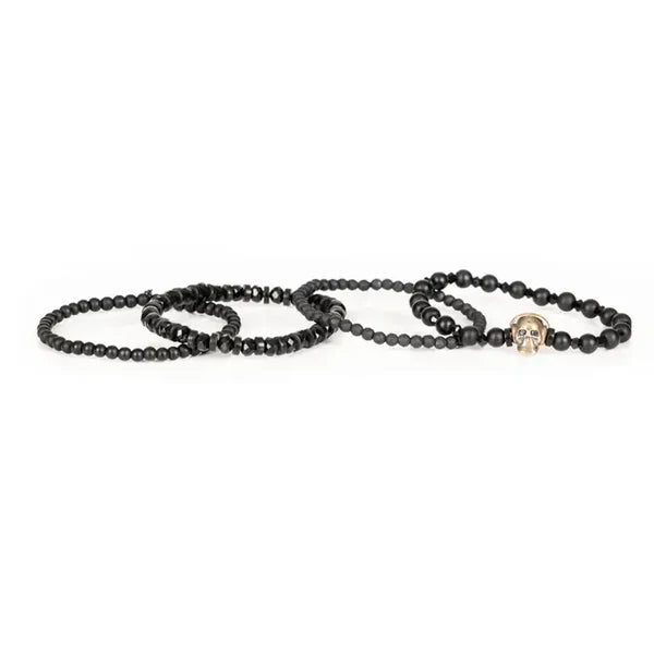 Black layered men’s bracelet set featuring matte black beads, faceted black crystal beads, and an antique gold skull centerpiece on a white background.