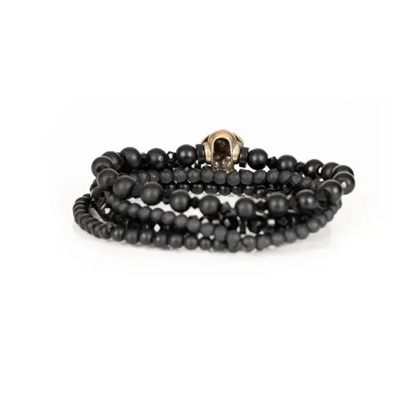 Black layered men’s bracelet set featuring matte black beads, faceted black crystal beads, and an antique gold skull centerpiece on a white background.