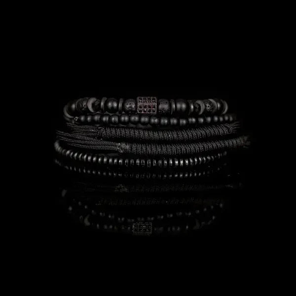 Men's layered black bracelet set featuring matte black beads, lava stone beads, hematite spacers, braided cord strands, and a black pavé cubic zirconia square centerpiece in a sleek modern luxury design.