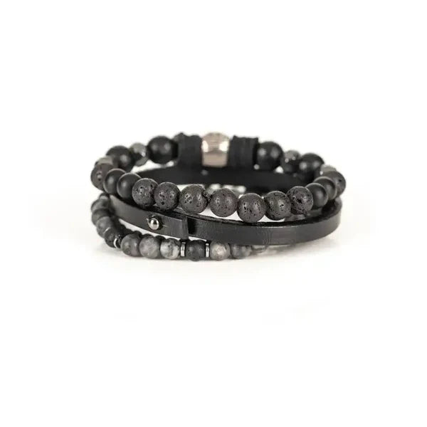 Layered men’s bracelet set featuring black faceted stone beads, a black leather band, lava stone beads, gray natural stone beads, and a silver skull centerpiece, displayed on a white background.