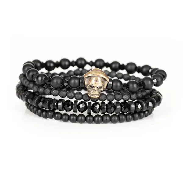 Black layered men’s bracelet set featuring matte black beads, faceted black crystal beads, and an antique gold skull centerpiece on a white background.