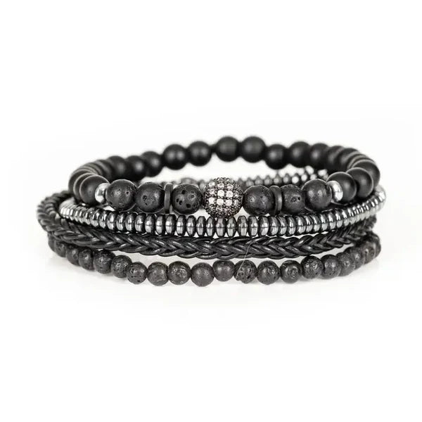 Black layered men’s bracelet with lava stone beads, braided leather detail, silver-tone accents, and crystal pavé centerpiece on a white background.