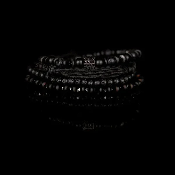 Men's layered black beaded bracelet set featuring matte black beads, lava stone beads, hematite spacers, braided cord strands, and a black pavé cubic zirconia accent bead for a modern luxury look.