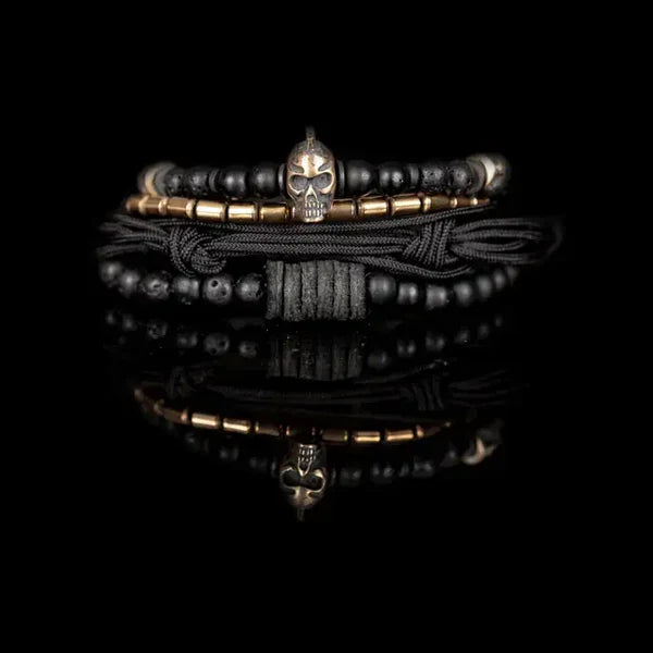 Black layered men’s bracelet with matte black beads, lava stone accents, braided cord wraps, bronze-tone metal beads, and a Spartan skull centerpiece on a white background.
