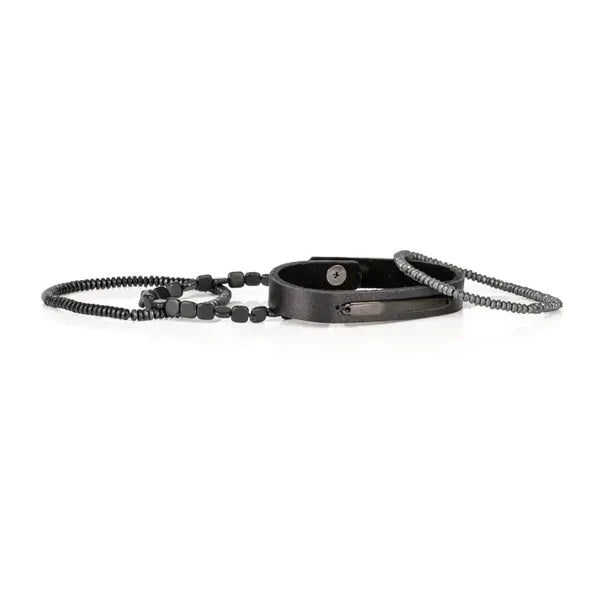 Layered men’s bracelet set featuring a black leather band with a black metal plate, matte hematite cube beads, and hematite disc beads in a sleek monochromatic design, displayed on a white background.