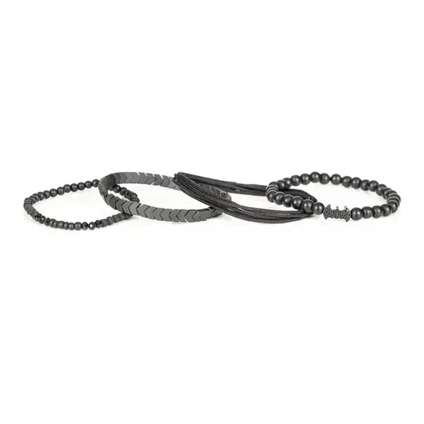 Men's layered black beaded bracelet set featuring matte black beads, hematite arrow-shaped beads, braided cord strands, faceted black crystal accents, and a black pavé bat-shaped centerpiece for a bold modern luxury style.