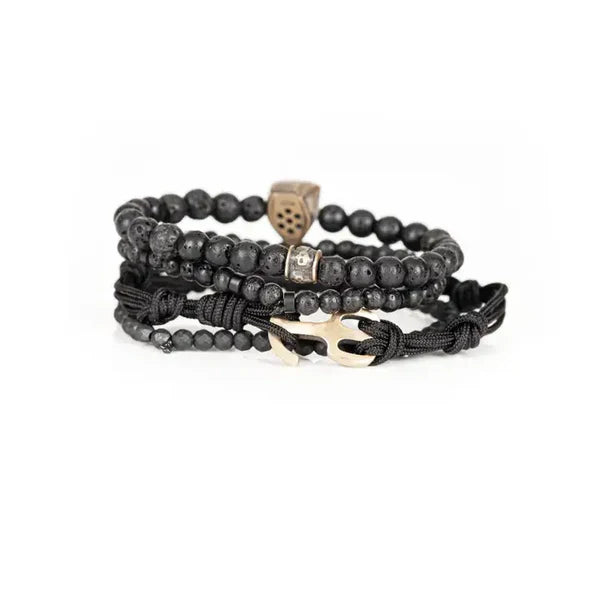 Black layered men’s bracelet featuring lava stone beads, faceted black stone accents, braided cord wraps, and an antique gold theatrical mask centerpiece on a white background.