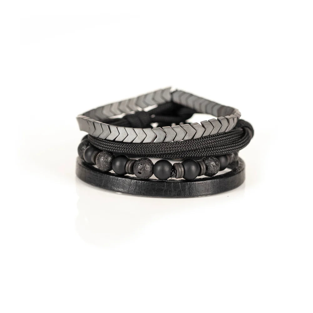 Men's handcrafted layered bracelet set featuring matte black onyx beads, black lava stone beads, black braided cord, genuine black leather band, and gunmetal hematite arrow-shaped beads. Premium minimalist men's bracelet stack photographed on a clean white background.