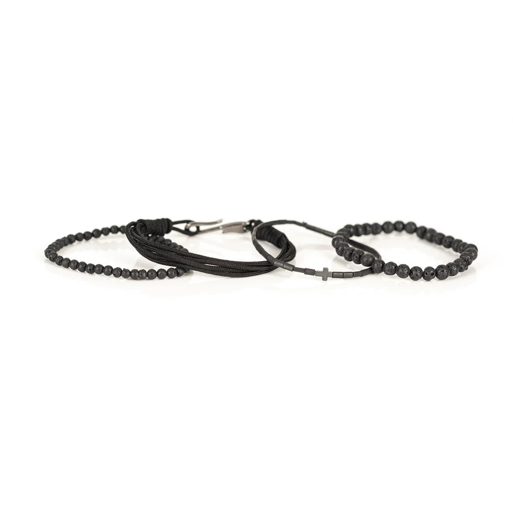 Men's handcrafted layered bracelet set featuring natural black lava stone beads, matte black hematite tube beads with a black cross accent, black braided cord, and black seed bead bracelets. Premium minimalist men's bracelet stack photographed on a clean white background.