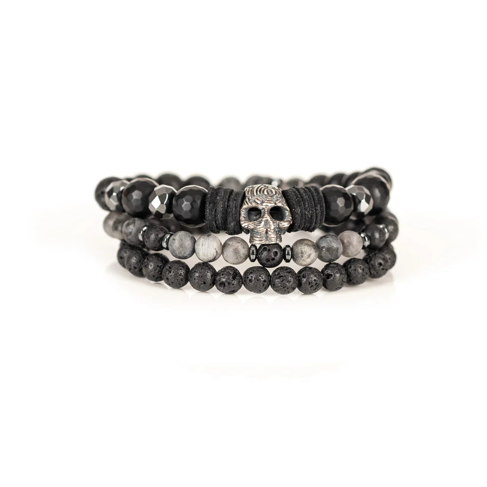 Men's handcrafted layered bracelet set featuring faceted black onyx beads, black lava stone beads, natural gray jasper gemstone beads, black hematite spacer beads, and a silver skull centerpiece with black leather accents. Premium stacked men's bracelet photographed on a clean white background.