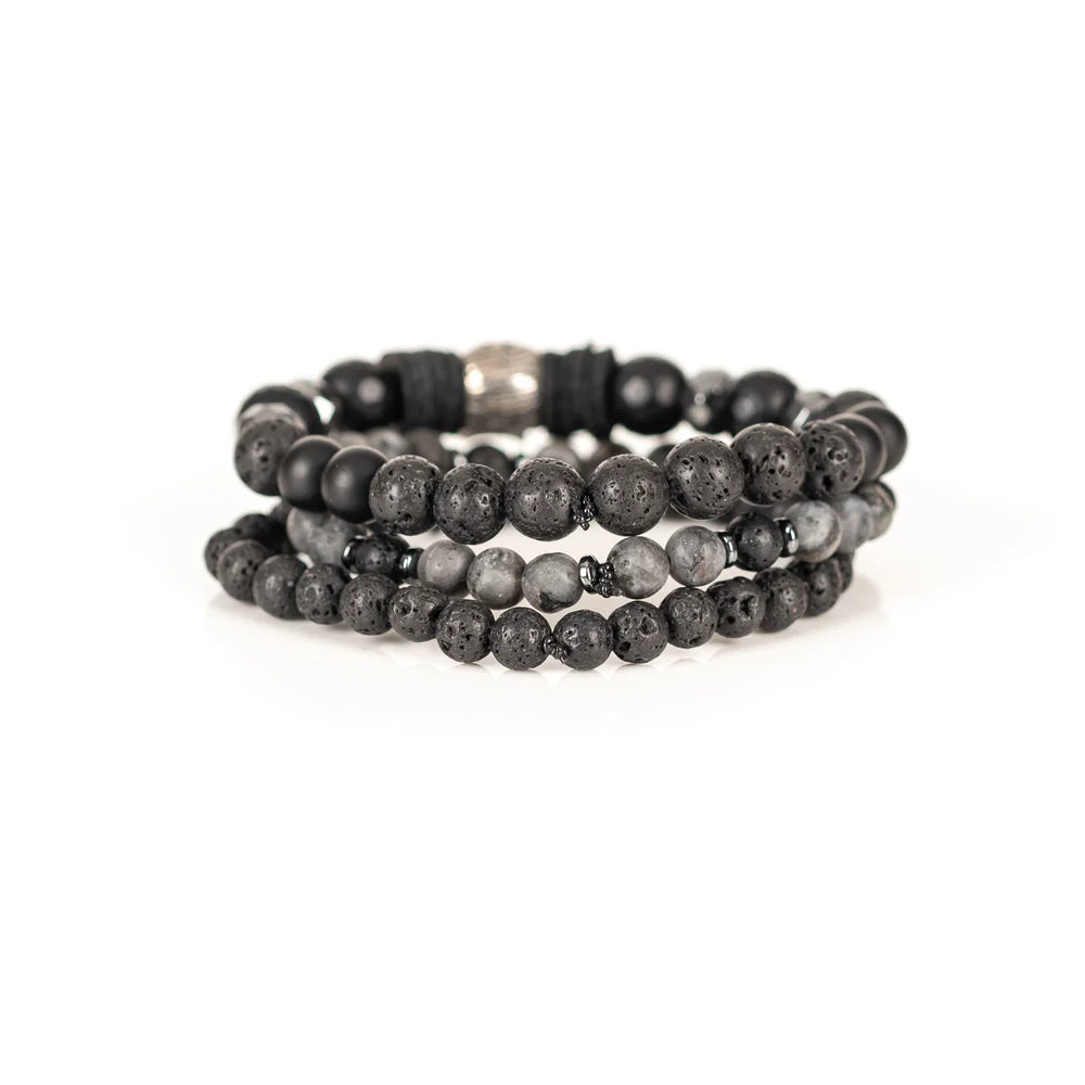 Men's handcrafted layered bracelet set featuring faceted black onyx beads, black lava stone beads, natural gray jasper gemstone beads, black hematite spacer beads, and a silver skull centerpiece with black leather accents. Premium stacked men's bracelet photographed on a clean white background.