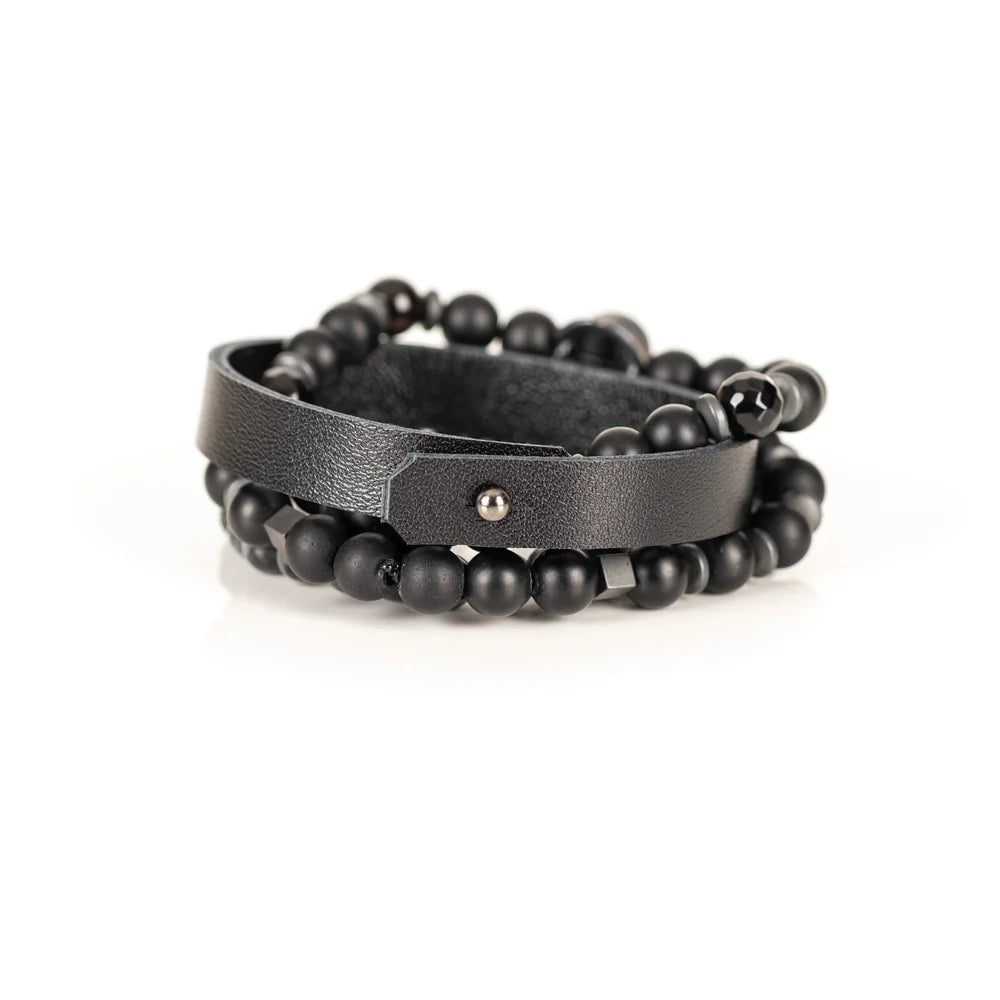 Men's handcrafted layered bracelet set featuring a black genuine leather cuff, matte black onyx beads, faceted black hematite beads, natural gray jasper gemstone beads, black hematite spacer beads, and a silver Spartan helmet centerpiece. Premium stacked men's bracelet photographed on a clean white background.