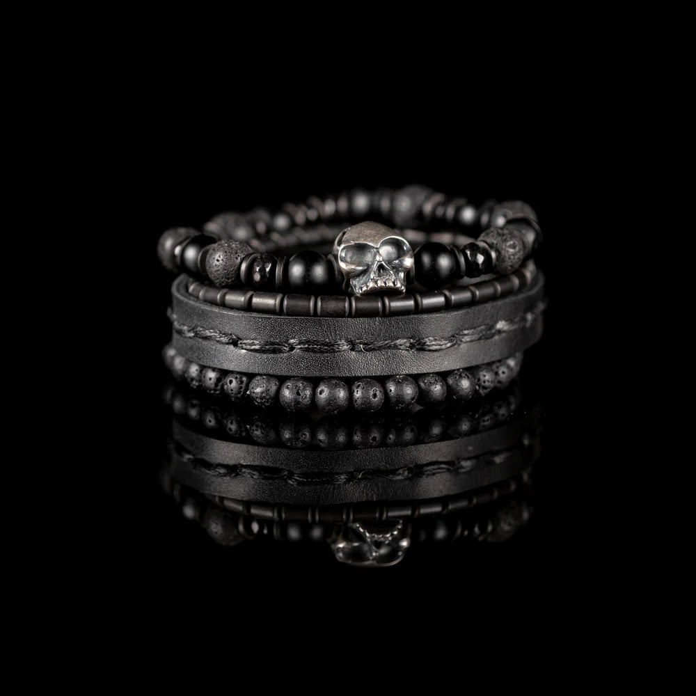 Men's handcrafted black leather wrap bracelet set featuring matte black onyx beads, natural lava stone beads, hematite accents, and a silver skull centerpiece. Premium layered men's bracelet stack photographed on a clean white background.