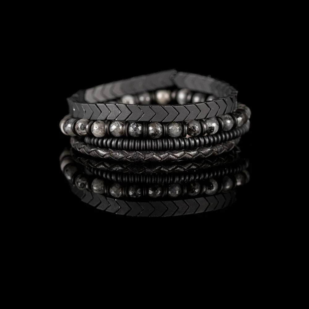 Men's handcrafted layered bracelet set featuring black leather wrap bands, braided leather, matte black hematite arrow beads, black spacer beads, and natural gray jasper gemstone beads. Premium men's stacked bracelet photographed on a clean white background.