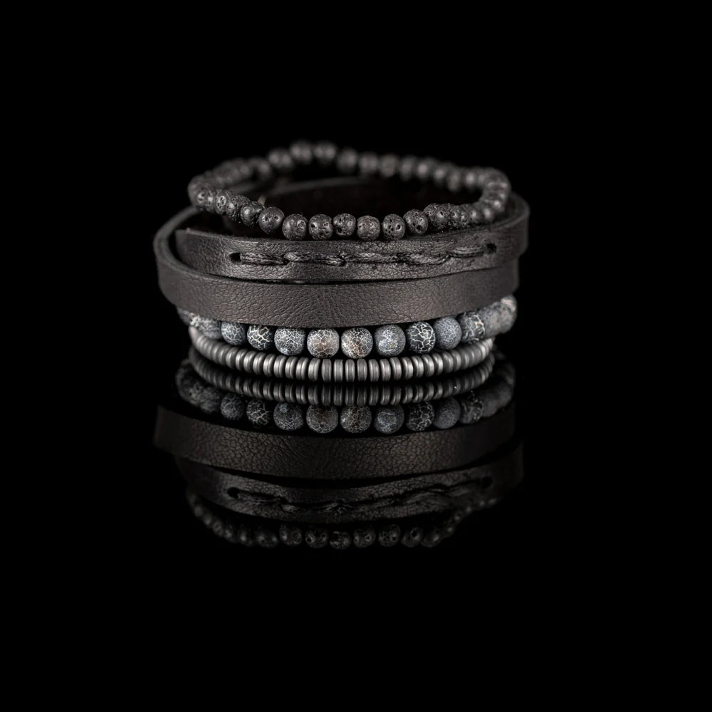 Men's handcrafted layered bracelet set featuring a black genuine leather wrap cuff, black lava stone beads, natural gray crackle agate gemstone beads, matte gray heishi disc beads, and premium stitched leather detailing. Luxury men's stacked bracelet photographed on a clean white background.