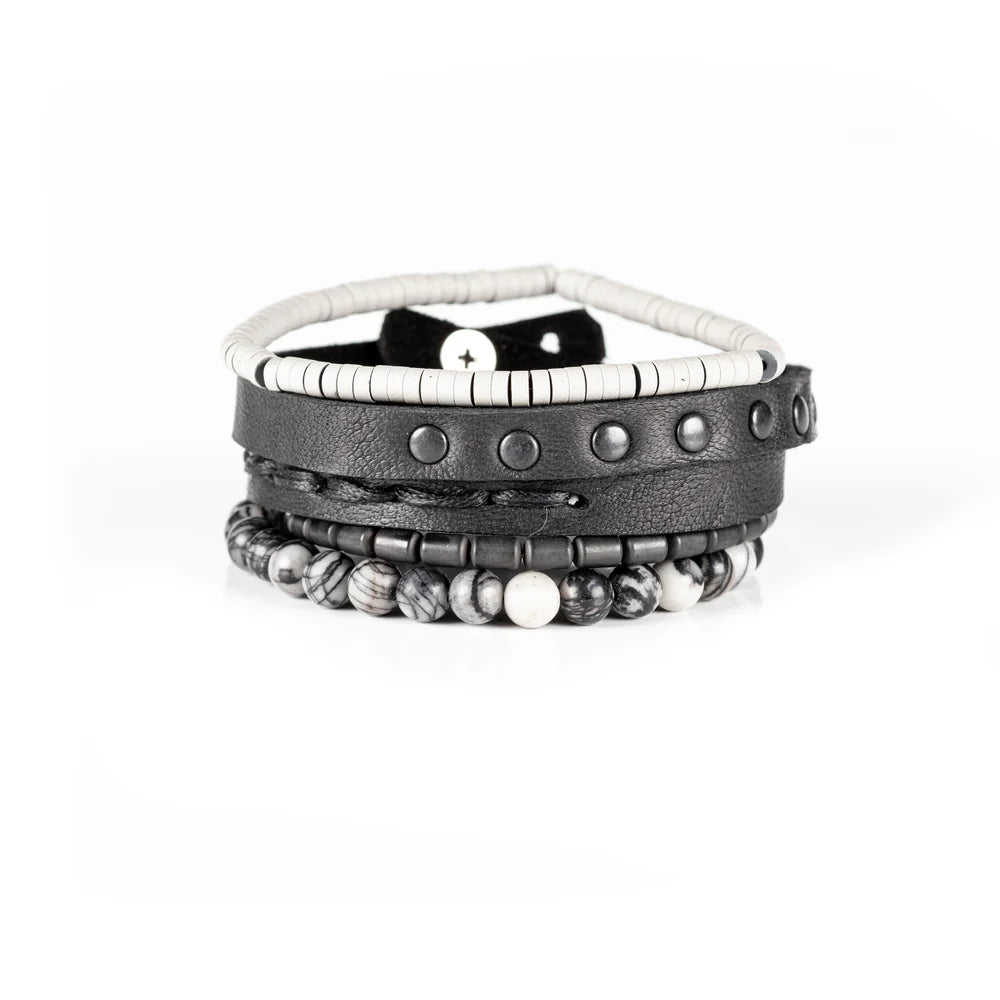 Men's handcrafted layered bracelet set featuring a black genuine leather wrap bracelet with gunmetal studs, white heishi disc beads, matte gunmetal hematite spacers, and natural black-and-white Picasso jasper gemstone beads. Premium stacked men's bracelet photographed on a clean white background.