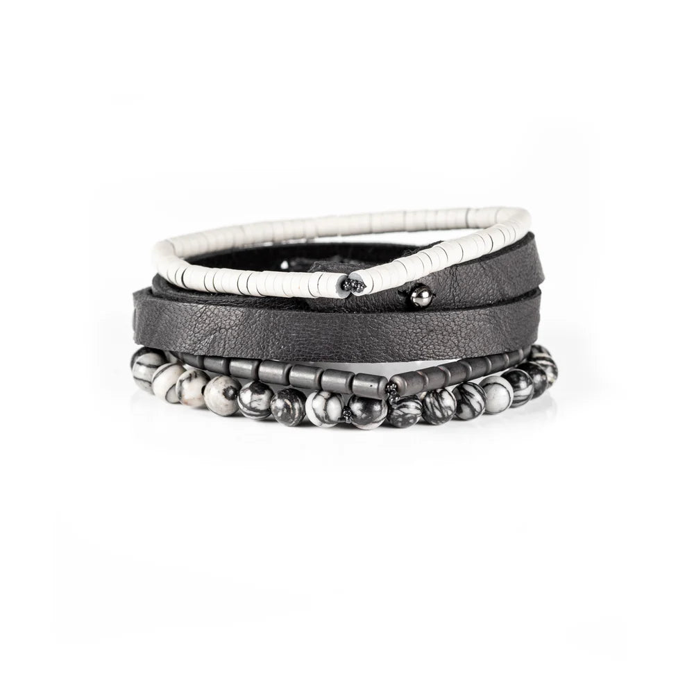 Men's handcrafted layered bracelet set featuring a black genuine leather wrap bracelet with gunmetal studs, white heishi disc beads, matte gunmetal hematite spacers, and natural black-and-white Picasso jasper gemstone beads. Premium stacked men's bracelet photographed on a clean white background.