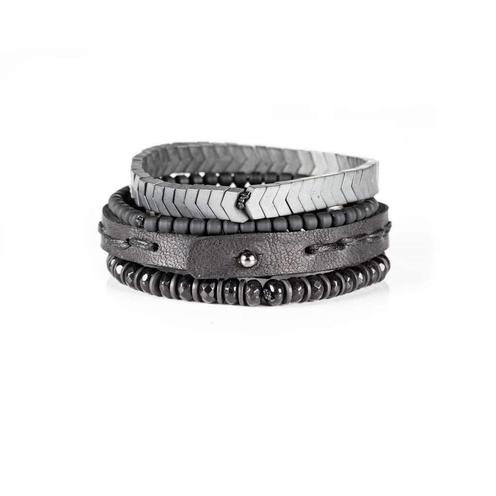 Men's handcrafted layered bracelet set featuring silver hematite arrow-shaped beads, black seed beads, a black leather wrap bracelet with matte gunmetal studs, and faceted black hematite beads. Premium minimalist men's bracelet stack photographed on a clean white background.