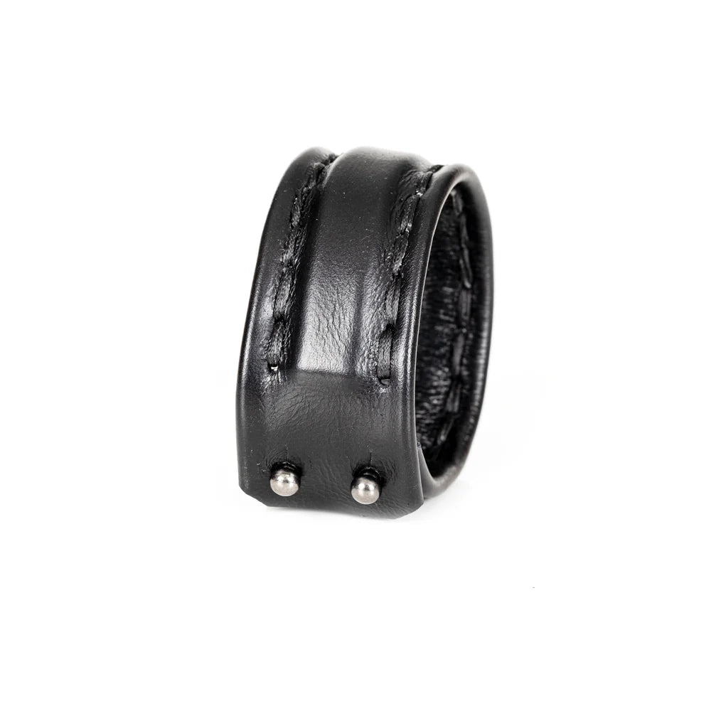 Black genuine leather cuff bracelet with a wide padded center panel and hand-stitched leather straps, photographed on a black reflective background with a luxury editorial look.
